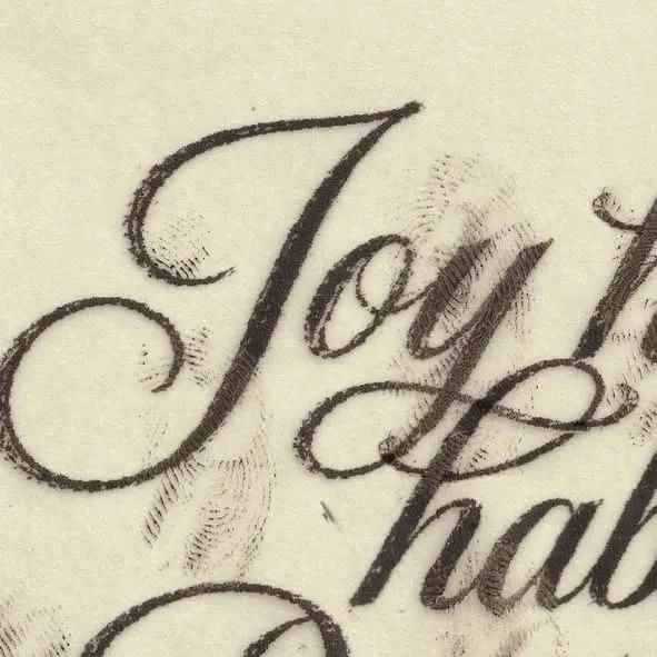 Close-up of vintage script lettering reading Joy on aged cream paper