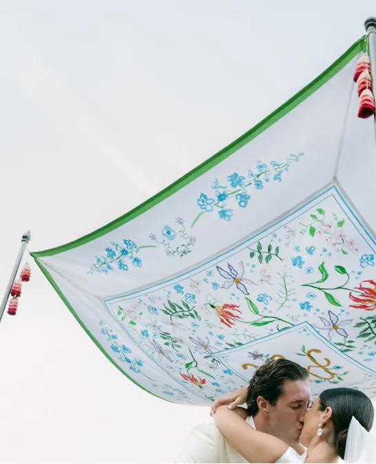 Couple kissing under a floral-embroidered chuppah with green trim and red tassels
