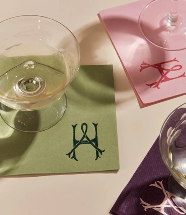 Monogrammed cocktail napkins in sage, pink, and purple beneath champagne glasses