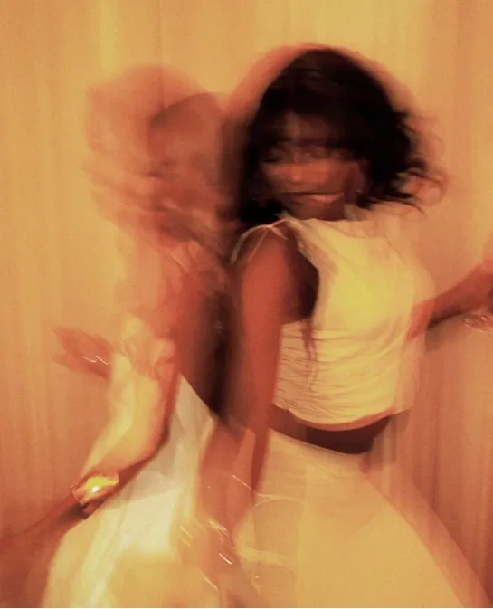 Motion-blurred photo of a woman dancing in white against warm golden light