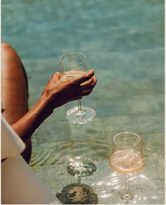 Hand holding a glass of white wine poolside beside a glass of rosé